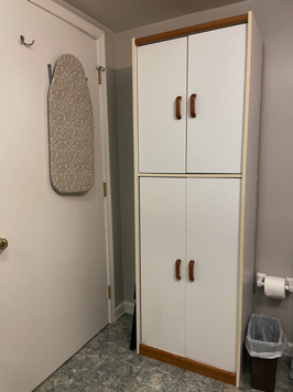 Behind bathroom door is counter ironing board and a tall cabinet for storage and towels.